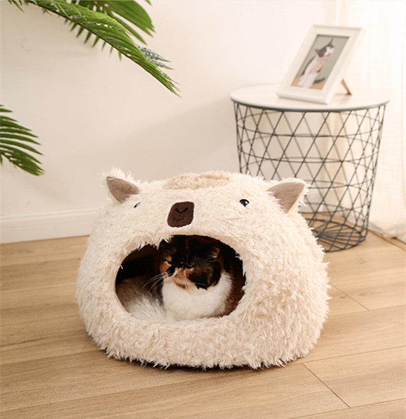 Cat lying inside a fluffy white cat bed shaped like a bear on a wooden floor.