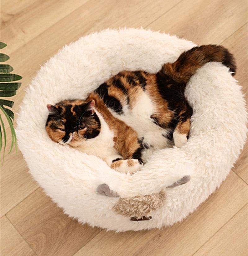 Calico cat sleeping in a fluffy white pet bed on a wooden floor.