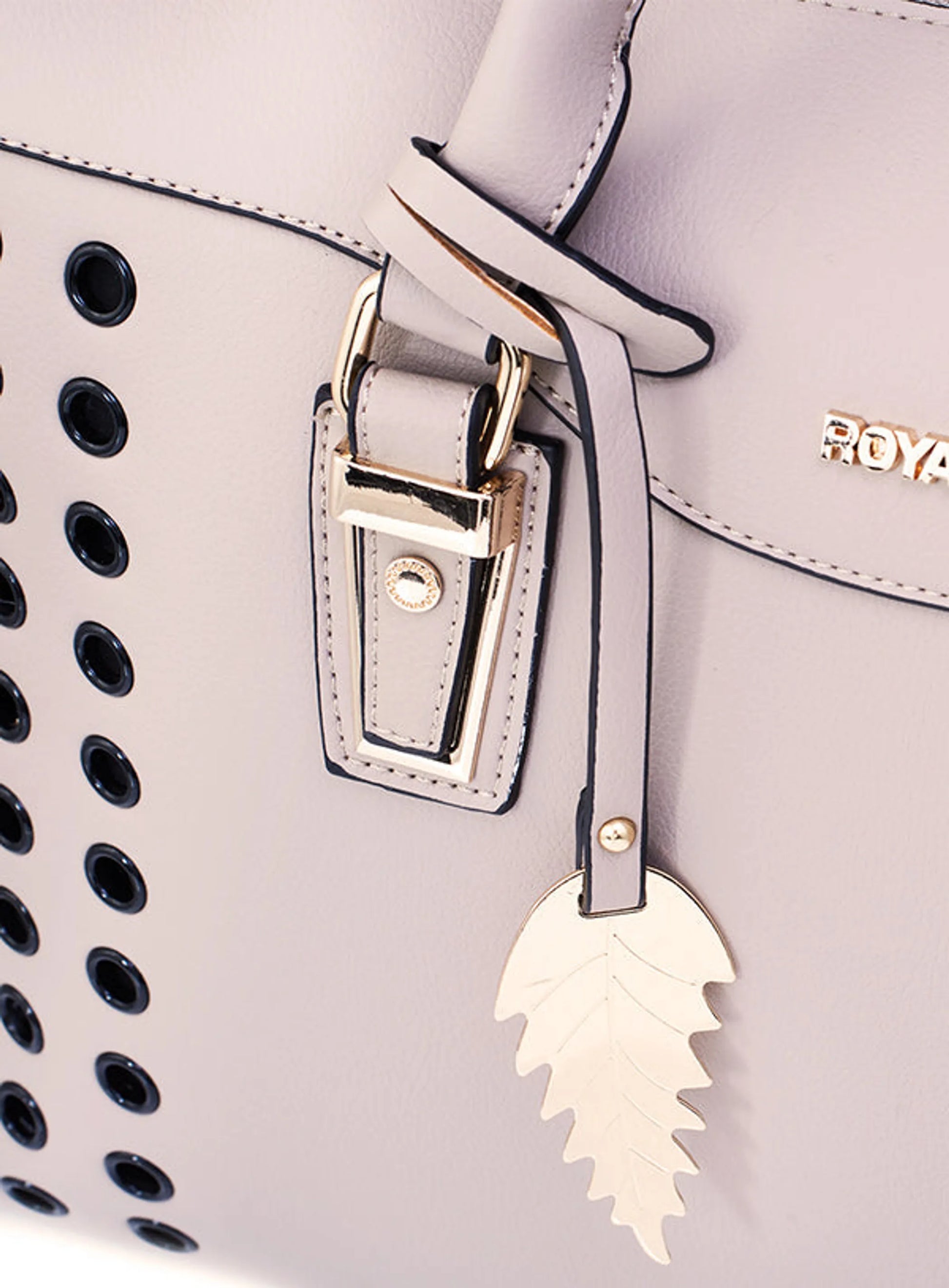 Close-up of a light blush handbag with black perforations and a gold clasp, featuring the brand 'ROYAL'.
